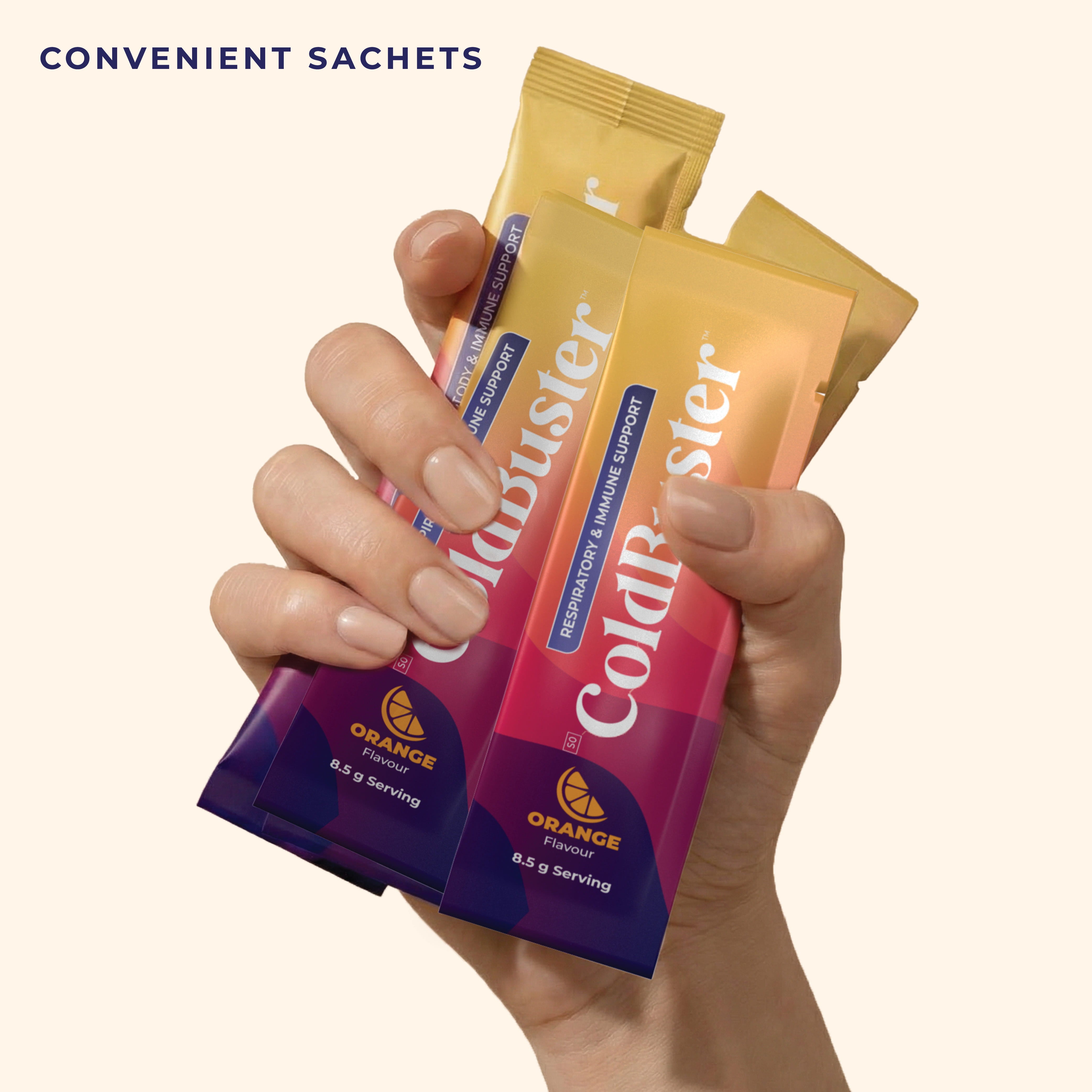 Hand holding multiple ColdBuster orange flavour respiratory and immune support sachets, each an 8.5g single-serving sachet for on-the-go use.