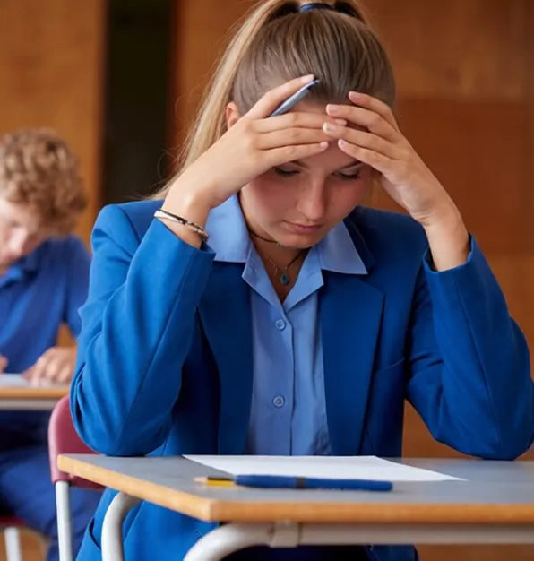 Student in a school blazer holding her head over an exam paper