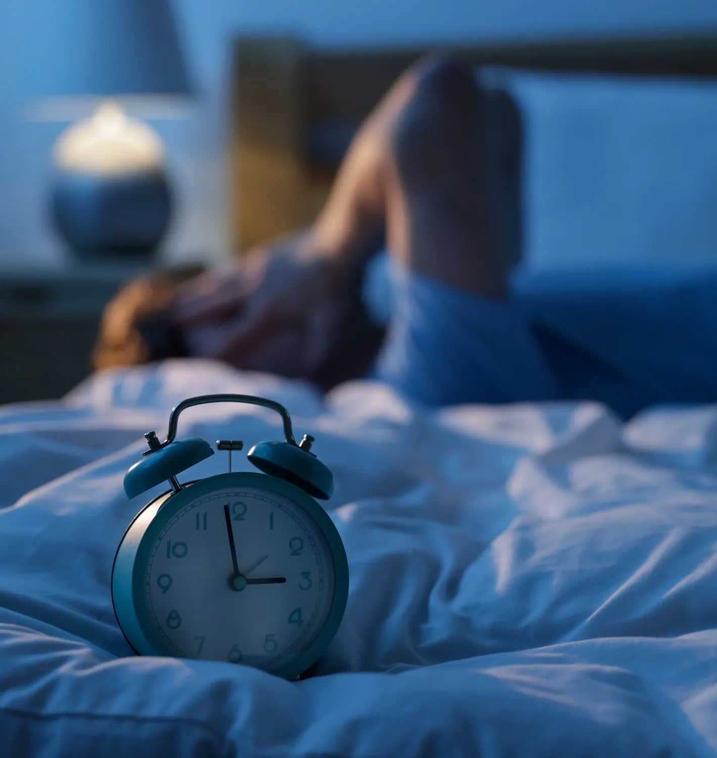 Alarm clock on a bed at night while a teenager lies awake