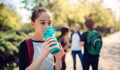 Schoolgirl wearing red backpack drinking water at schoolyard on a sunny day